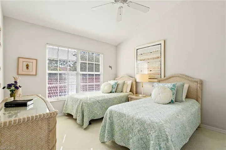 Bright bedroom featuring a large window, neutral wall paint, and sloped ceiling with a ceiling fan