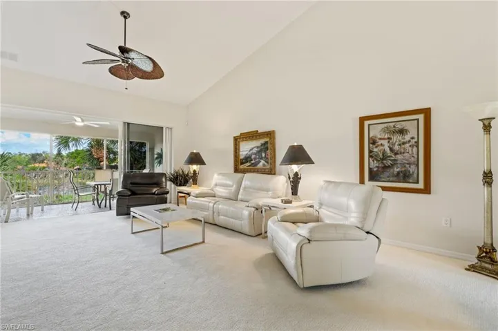 Living area featuring a vaulted ceiling with a ceiling fan, light-toned carpeting, and sliding glass doors opening to a screened balcony