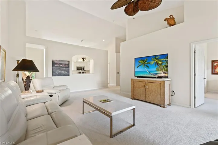 Spacious living area featuring vaulted ceilings, a ceiling fan, and light-toned carpeting