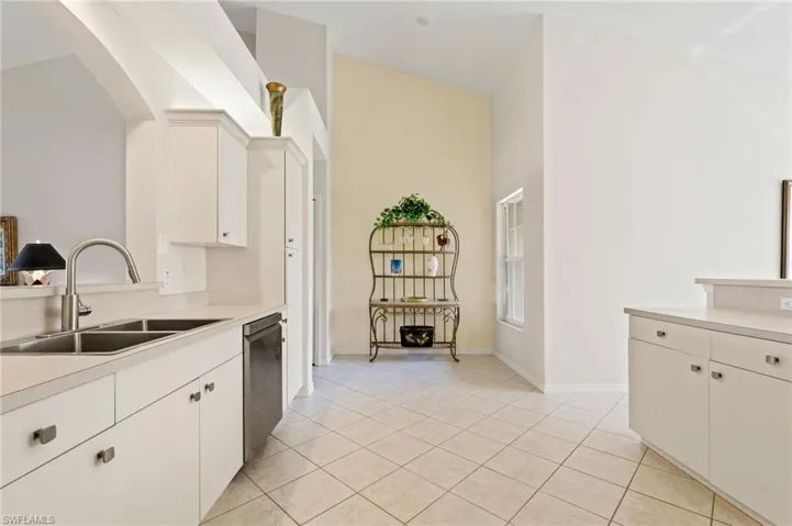 Kitchen area featuring a double basin stainless steel sink with a high-arc faucet, white cabinetry, integrated dishwasher, and light-toned countertops