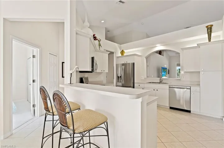 Bright kitchen featuring a breakfast bar, white cabinetry, stainless steel appliances, and tile flooring