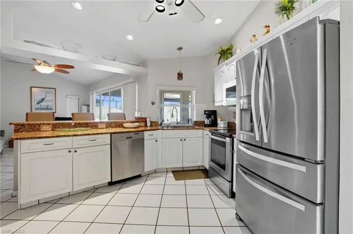 Kitchen with stainless steel appliances, vaulted ceiling, white cabinets, light tile patterned floors, and a ceiling fan