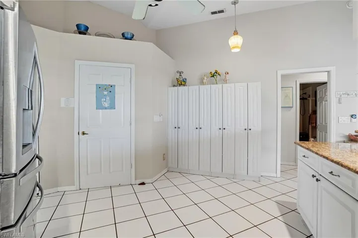 Kitchen featuring stainless steel refrigerator with ice dispenser, white cabinets, light stone countertops, light tile patterned floors, and hanging light fixtures