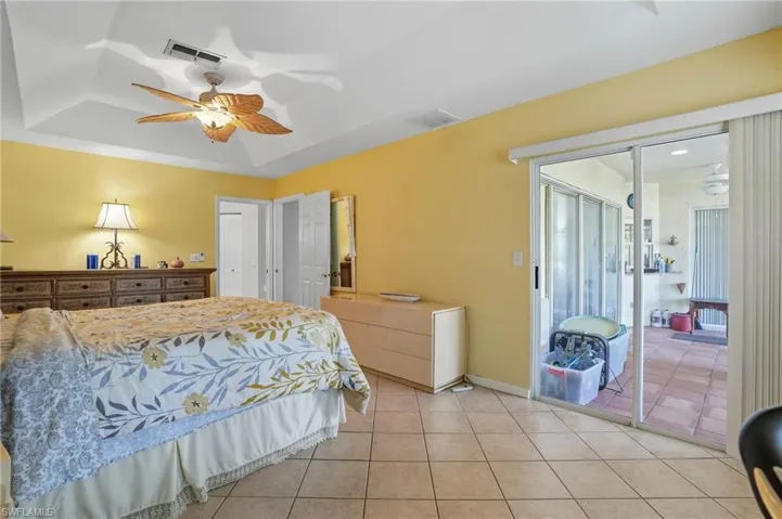 Bedroom with a raised ceiling, light tile patterned flooring, access to exterior, and ceiling fan
