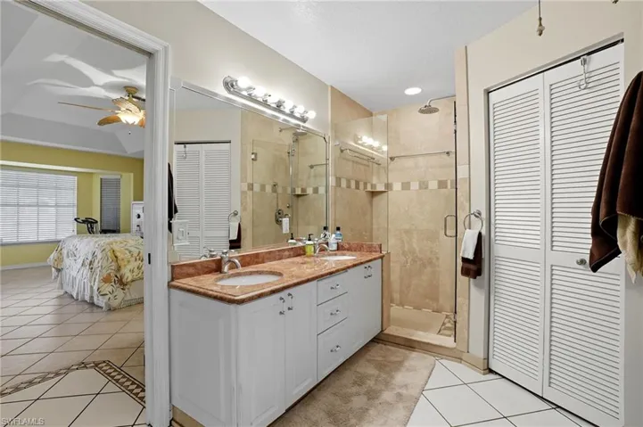 Full bath with a closet, light tile patterned floors, a shower stall, and double vanity