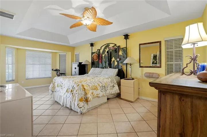 Bedroom with a raised ceiling, light tile patterned floors, and a ceiling fan