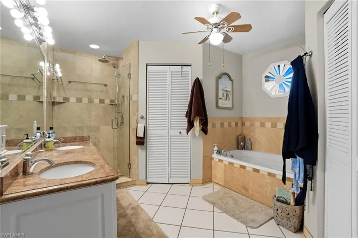 Full bath with a closet, light tile patterned flooring, a garden tub, a stall shower, and double vanity