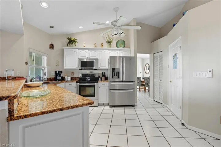 Kitchen with appliances with stainless steel finishes, white cabinetry, hanging light fixtures, dark stone counters, and light tile patterned floors