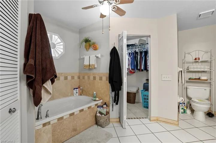 Bathroom with a bath, light tile patterned floors, a spacious closet, and ceiling fan