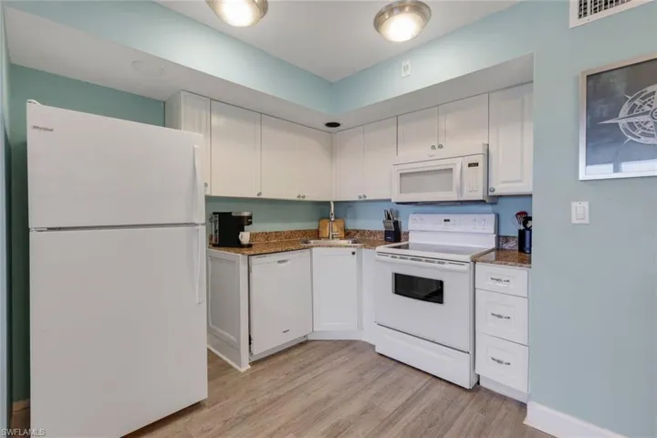Kitchen featuring white appliances, white cabinets, dark stone counters, sink, and light hardwood / wood-style flooring