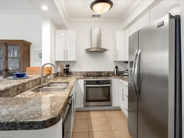 Kitchen featuring stainless steel appliances, range hood, dark stone counters, ornamental molding, and white cabinets