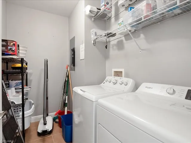 Laundry room featuring light tile patterned flooring, washing machine and clothes dryer, and electric panel
