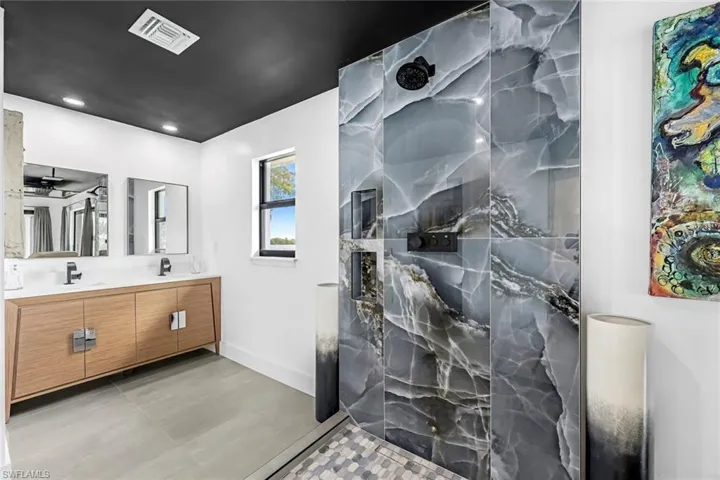 Bathroom with a shower, vanity with extensive cabinet space, dual sinks, ceiling fan, and tile floors