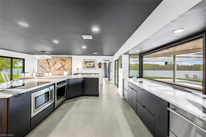Kitchen with appliances with stainless steel finishes, light stone counters, a water view, decorative light fixtures, and light tile flooring