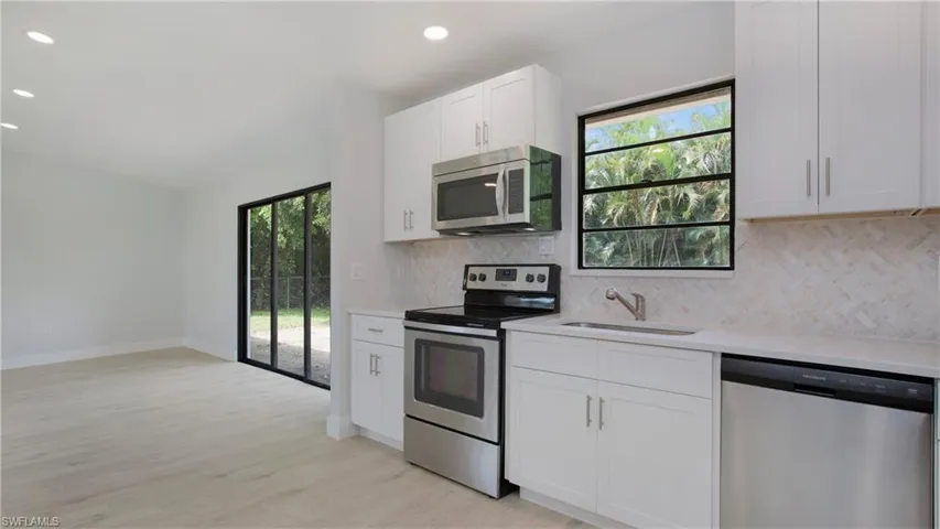 Kitchen featuring light hardwood / wood-style flooring, stainless steel appliances, sink, decorative backsplash, and white cabinets