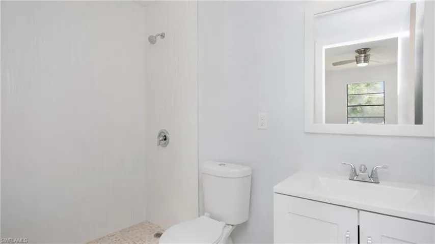 Bathroom featuring ceiling fan, toilet, a tile shower, and vanity