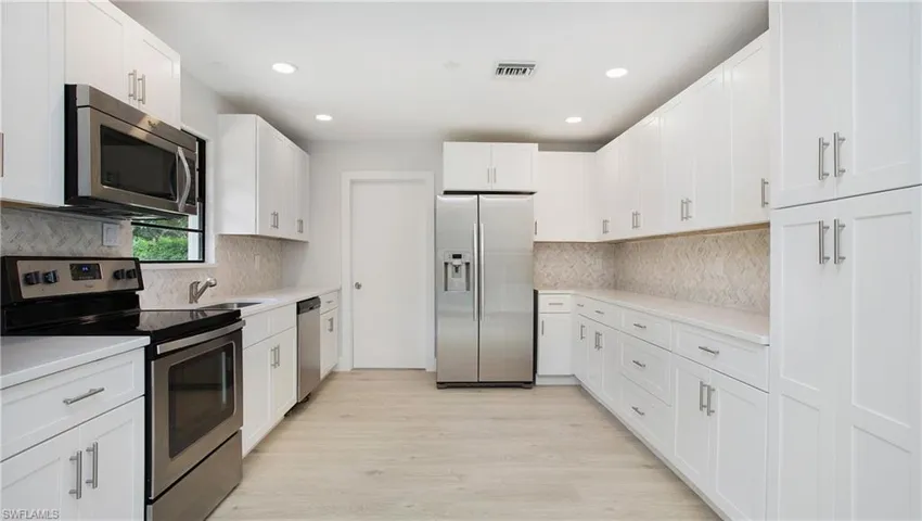 Kitchen featuring white cabinets, light wood-type flooring, stainless steel appliances, sink, and tasteful backsplash