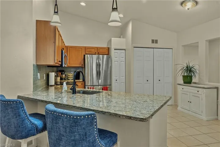 Kitchen with light stone counters, appliances with stainless steel finishes, backsplash, a peninsula, and vaulted ceiling