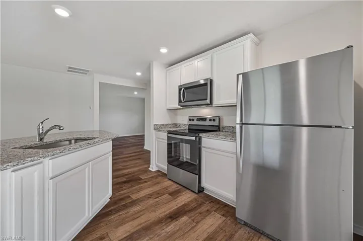 Kitchen featuring dark hardwood / wood-style floors, light stone countertops, white cabinets, sink, and appliances with stainless steel finishes