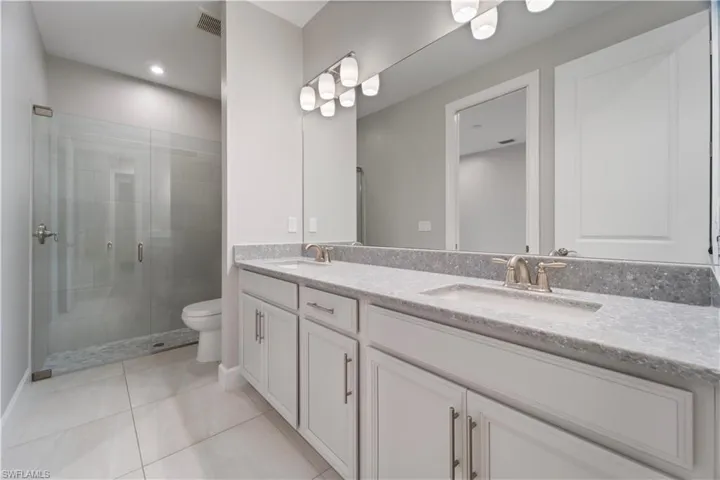 Bathroom with a shower with door, toilet, vanity, and tile patterned flooring