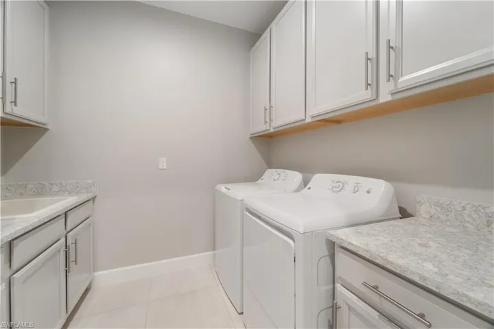 Clothes washing area with cabinets, light tile patterned floors, washer and clothes dryer, and sink