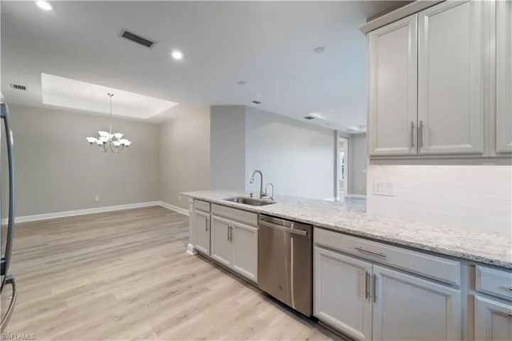 Kitchen featuring stainless steel dishwasher, a raised ceiling, sink, light hardwood / wood-style flooring, and light stone countertops