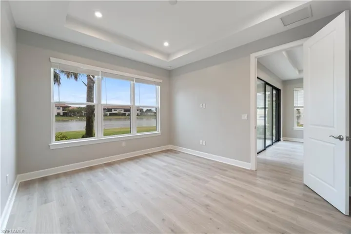 Unfurnished room with a raised ceiling, a water view, and light hardwood / wood-style floors