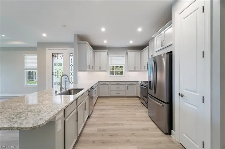 Kitchen with light hardwood / wood-style floors, kitchen peninsula, decorative backsplash, sink, and appliances with stainless steel finishes