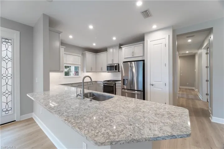 Kitchen with light wood-type flooring, kitchen peninsula, appliances with stainless steel finishes, and sink