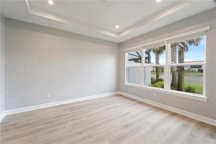 Spare room featuring light wood-type flooring, a water view, and a tray ceiling