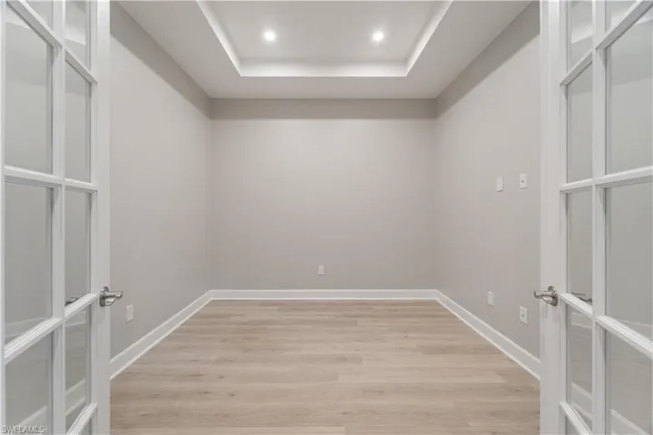 Spare room featuring a raised ceiling, french doors, and light hardwood / wood-style floors