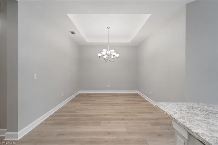 Unfurnished dining area featuring an inviting chandelier, a raised ceiling, and light wood-type flooring