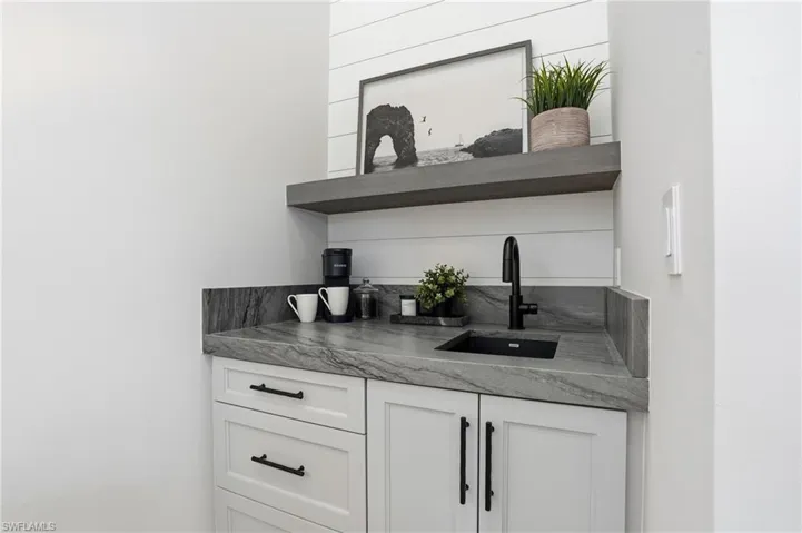 Bar area featuring open shelves, white cabinetry, and dark stone counters