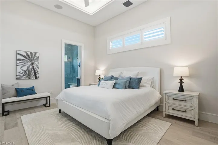 Bedroom with light wood finished floors, ensuite bath, and ceiling fan