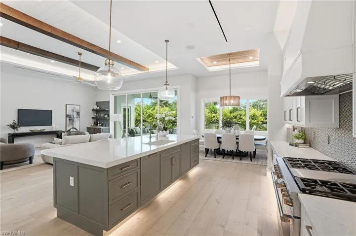 Two tone kitchen with two tone color scheme, a raised ceiling, pendant lighting, high end stove, and light wood-type flooring