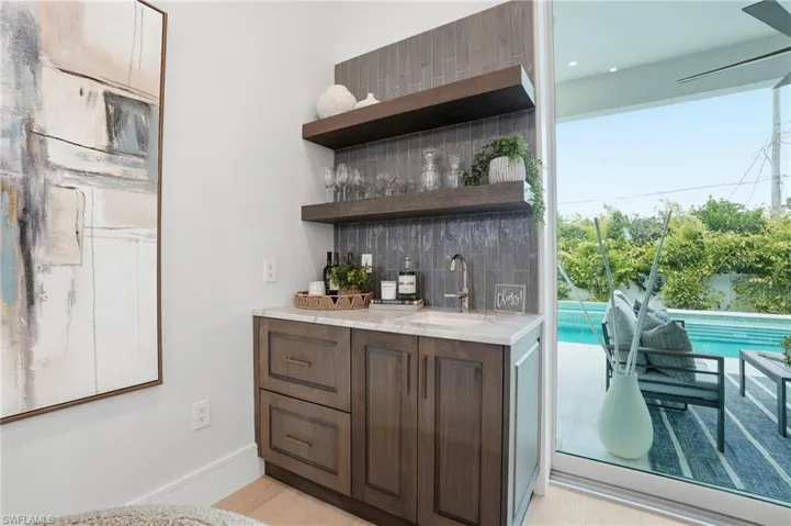 Indoor wet bar with open shelves, backsplash, dark wood finish cabinets, and light stone counters
