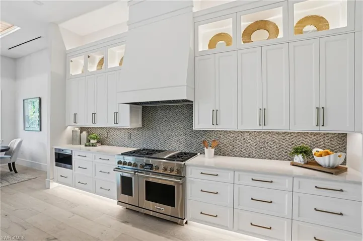Kitchen featuring white cabinetry, stainless steel appliances, light stone countertops, and glass insert cabinets