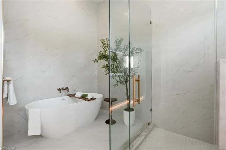 Bathroom featuring a soaking tub, a marble finish shower, and tile walls