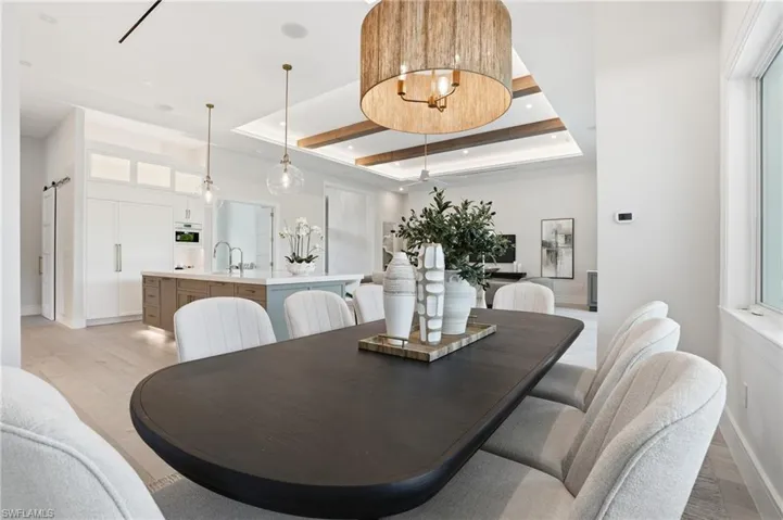 Dining area featuring a raised ceiling, light wood-type flooring, a barn door, and recessed lighting