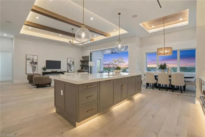 Kitchen with decorative light fixtures, light stone countertops, light wood finished floors, open floor plan, and a center island with sink