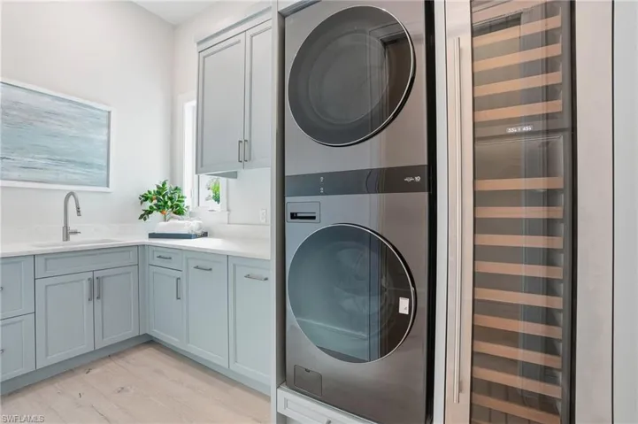 Laundry room with beverage cooler, stacked washer / dryer, and light wood finished floors