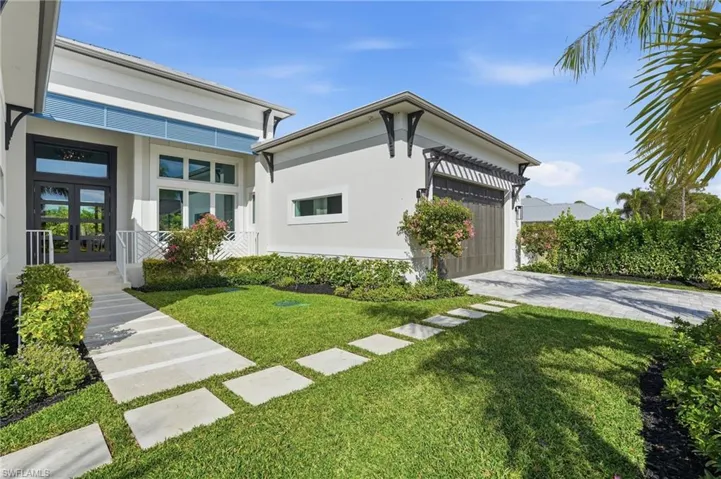 View of property exterior with stucco siding, driveway, a yard, and french doors