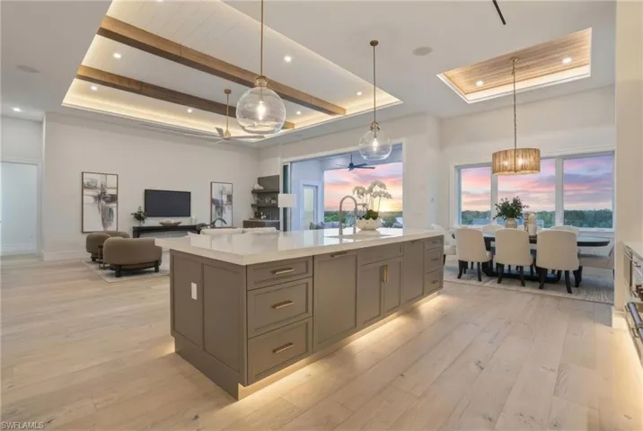 Kitchen featuring a raised ceiling, pendant lighting, light stone counters, light wood finished floors, and open floor plan