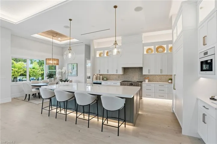 Two tone kitchen featuring a tray ceiling, decorative light fixtures, a breakfast bar, an island with sink, and light stone countertops