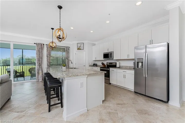 Kitchen with a breakfast bar area, a sink, ornamental molding, stainless steel appliances, and white cabinets