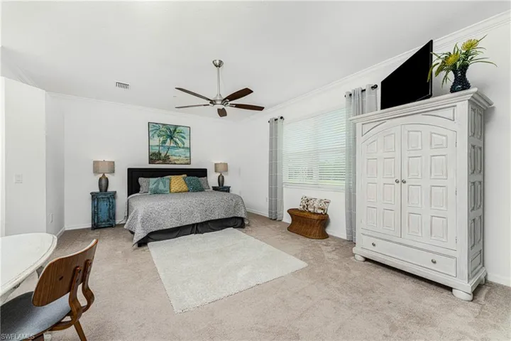 Bedroom with a ceiling fan, visible vents, baseboards, crown molding, and light colored carpet