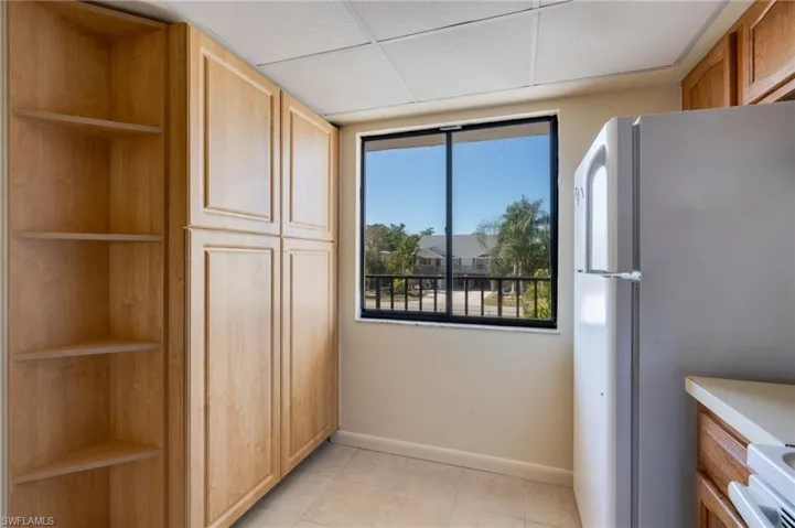 Kitchen with open shelves, freestanding refrigerator, stove, light tile patterned floors, and light countertops