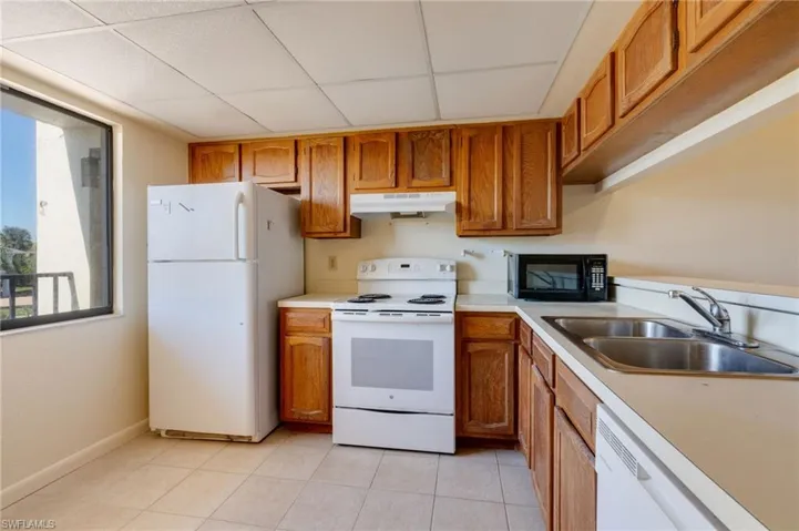 Kitchen with wood finish cabinets, white appliances, light countertops, and light tile patterned floors