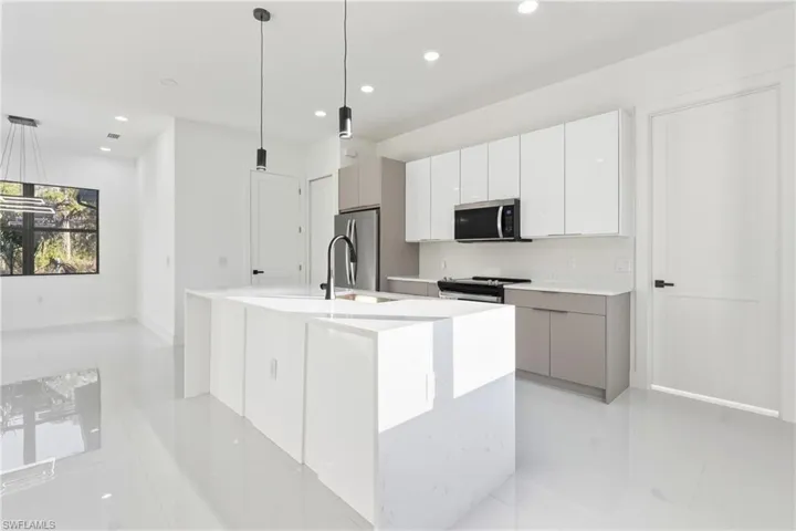 Kitchen with decorative light fixtures, white cabinetry, a center island with sink, modern cabinets, and stainless steel appliances