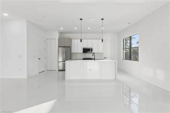 Kitchen with pendant lighting, stainless steel appliances, modern cabinets, a kitchen island with sink, and white cabinetry